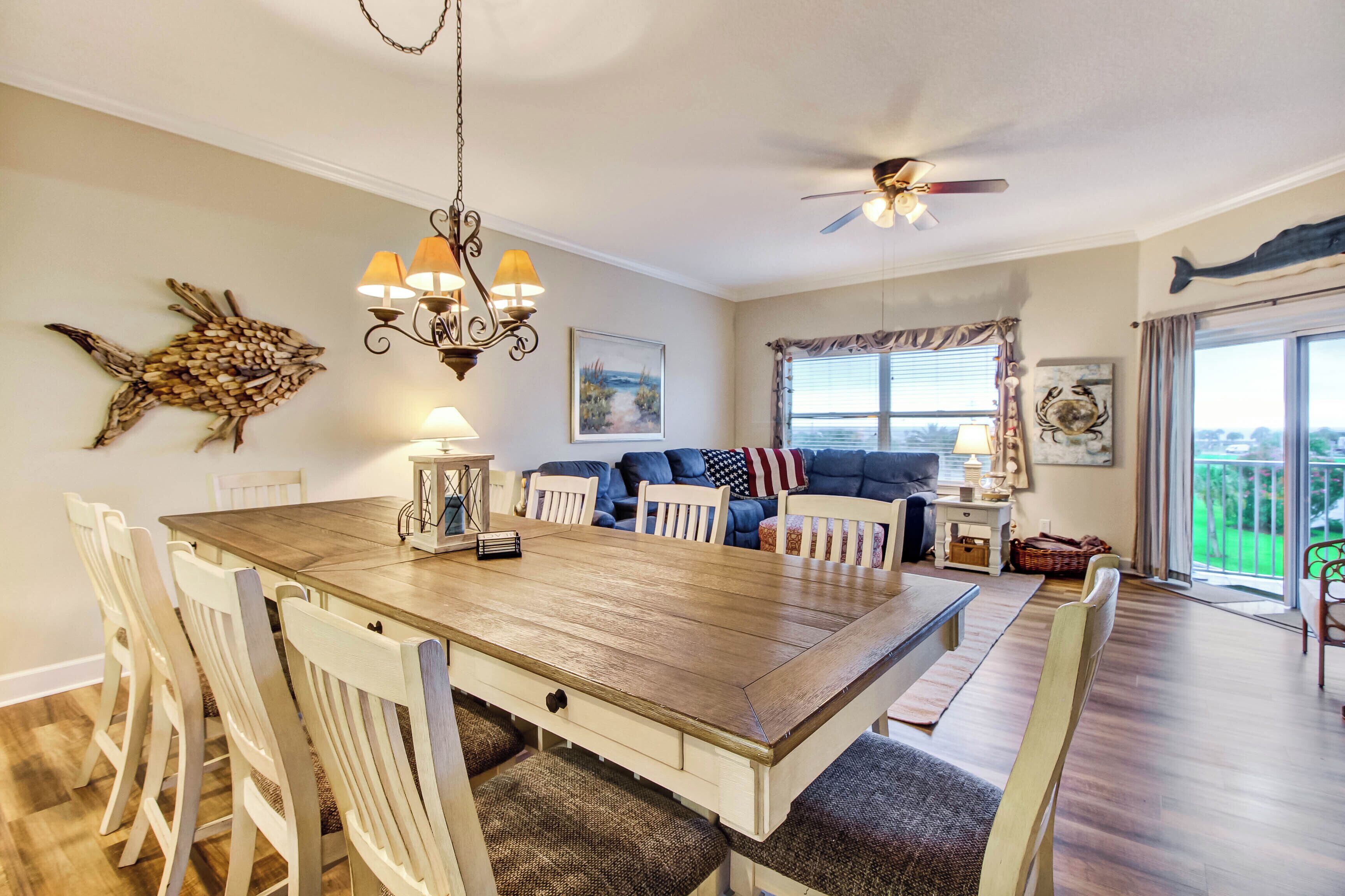 A dining area with a wooden table and chairs, a chandelier, and a ceiling fan.