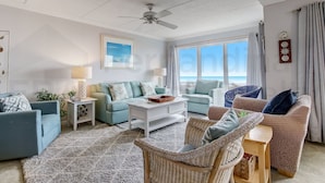 A living room with a ceiling fan, two sofas, a coffee table, and wicker chairs. - 109 Oceans of Amelia (Fernandina Beach)