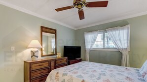 A bedroom with a bed, a dresser, a television, a ceiling fan, and a window with curtains. - 109 Oceans of Amelia (Fernandina Beach)