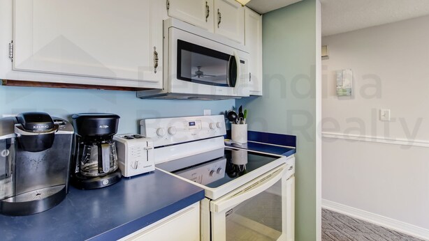 A compact kitchen with white cabinets, a microwave, a coffee maker, a toaster, and a small oven. - 109 Oceans of Amelia (Fernandina Beach)