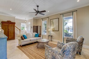 A living room with a sofa, patterned armchairs, a coffee table, a ceiling fan, and a view through a window. - 1016 San Fernando Street (Fernandina Beach)