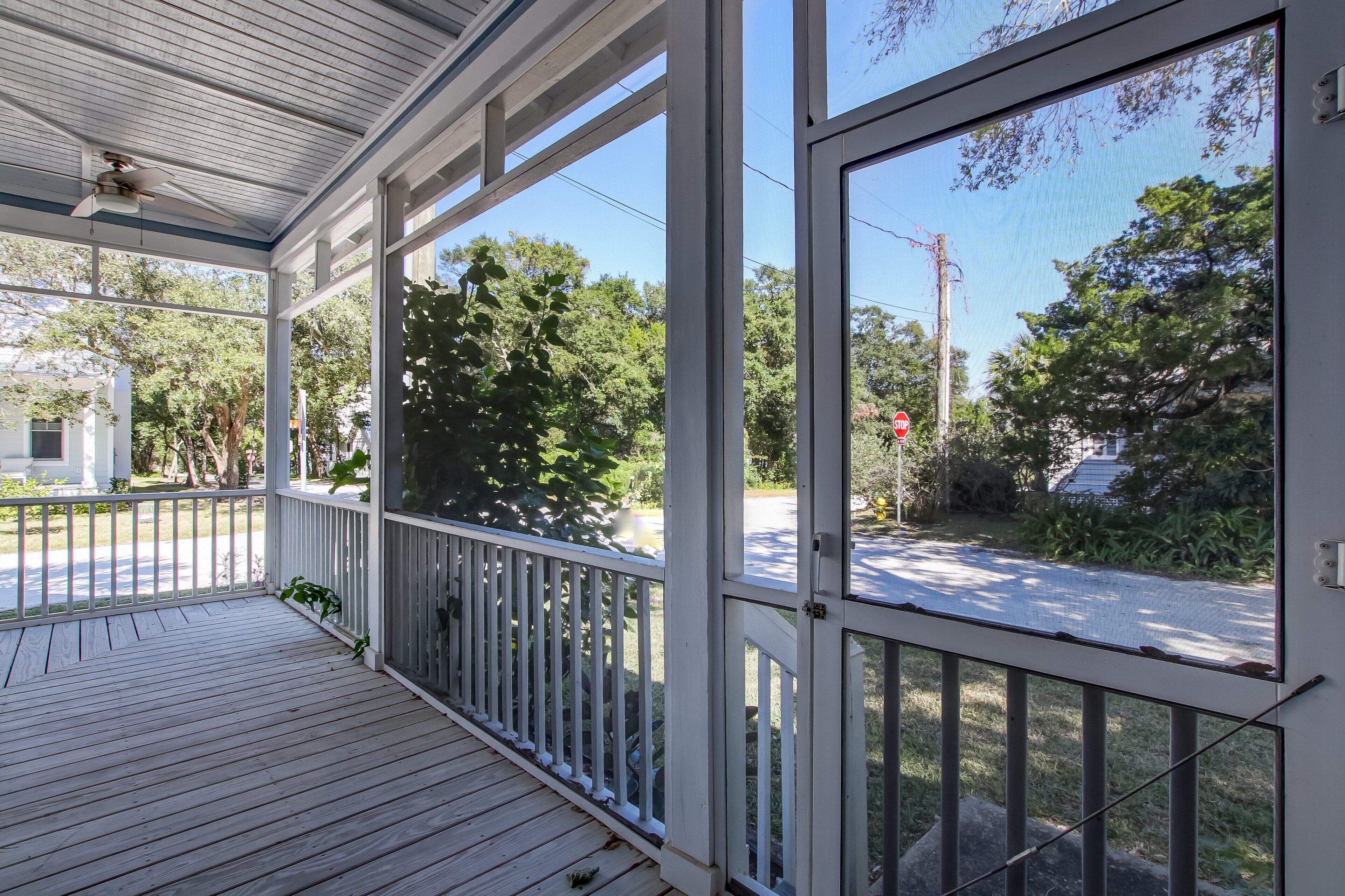 A covered porch with a ceiling fan, white railings, and a view of a street with trees and a stop sign.