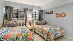 Camera da letto con due letti, un comodino, una lampada e un cartello a parete che indica un bar e una spiaggia.