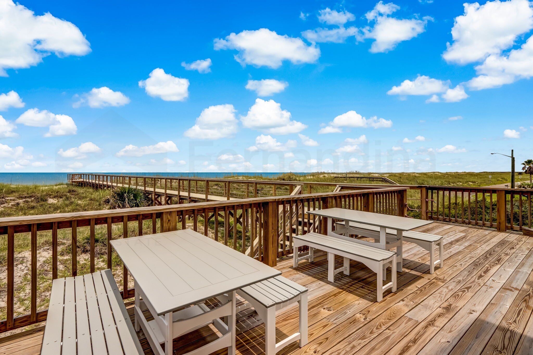 A wooden deck with picnic tables and benches overlooking a beach and ocean.