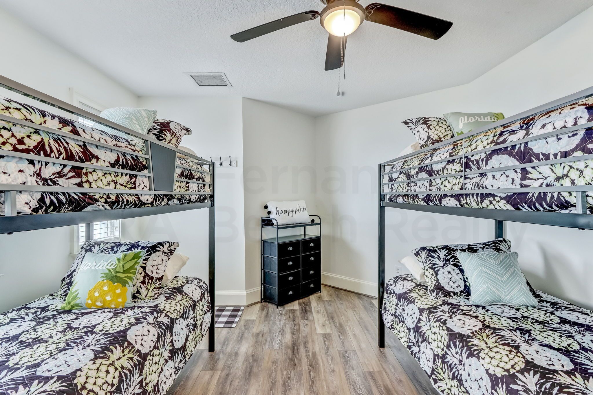 Une chambre avec des lits superposés, un ventilateur de plafond, un petit espace de rangement et une fenêtre avec des stores.
