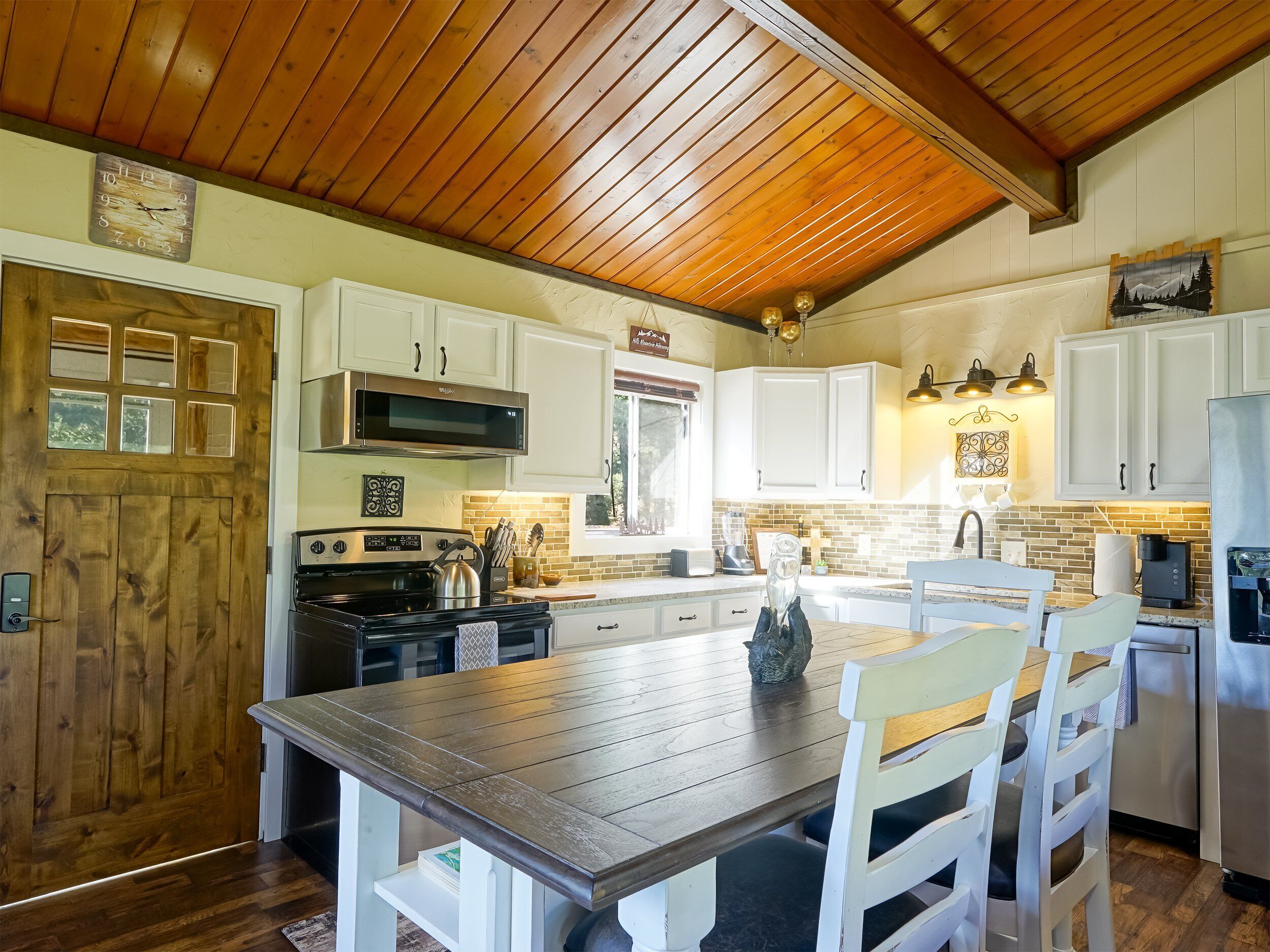 A kitchen with wooden ceiling, white cabinets, a wooden dining table, and a stove.