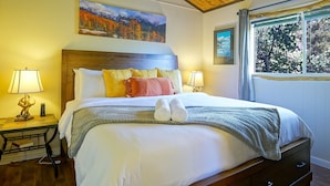 A well-lit bedroom with a wooden ceiling, a large bed with multiple pillows, bedside tables with lamps, and a painting of a mountainous landscape. - 181 Horseshoe (Divide)