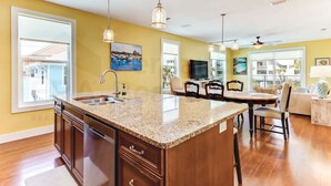 A kitchen with granite countertops, wooden cabinets, a large island, pendant lighting, and a dining area with chairs and a table. - 391 South Fletcher A&B (Fernandina Beach)