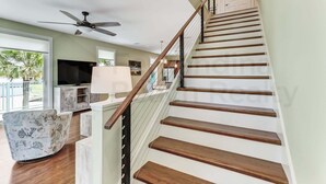 A staircase with wooden steps and a metal railing, a ceiling fan, a flat-screen TV, and a view of the outdoors. - 391 South Fletcher A&B (Fernandina Beach)