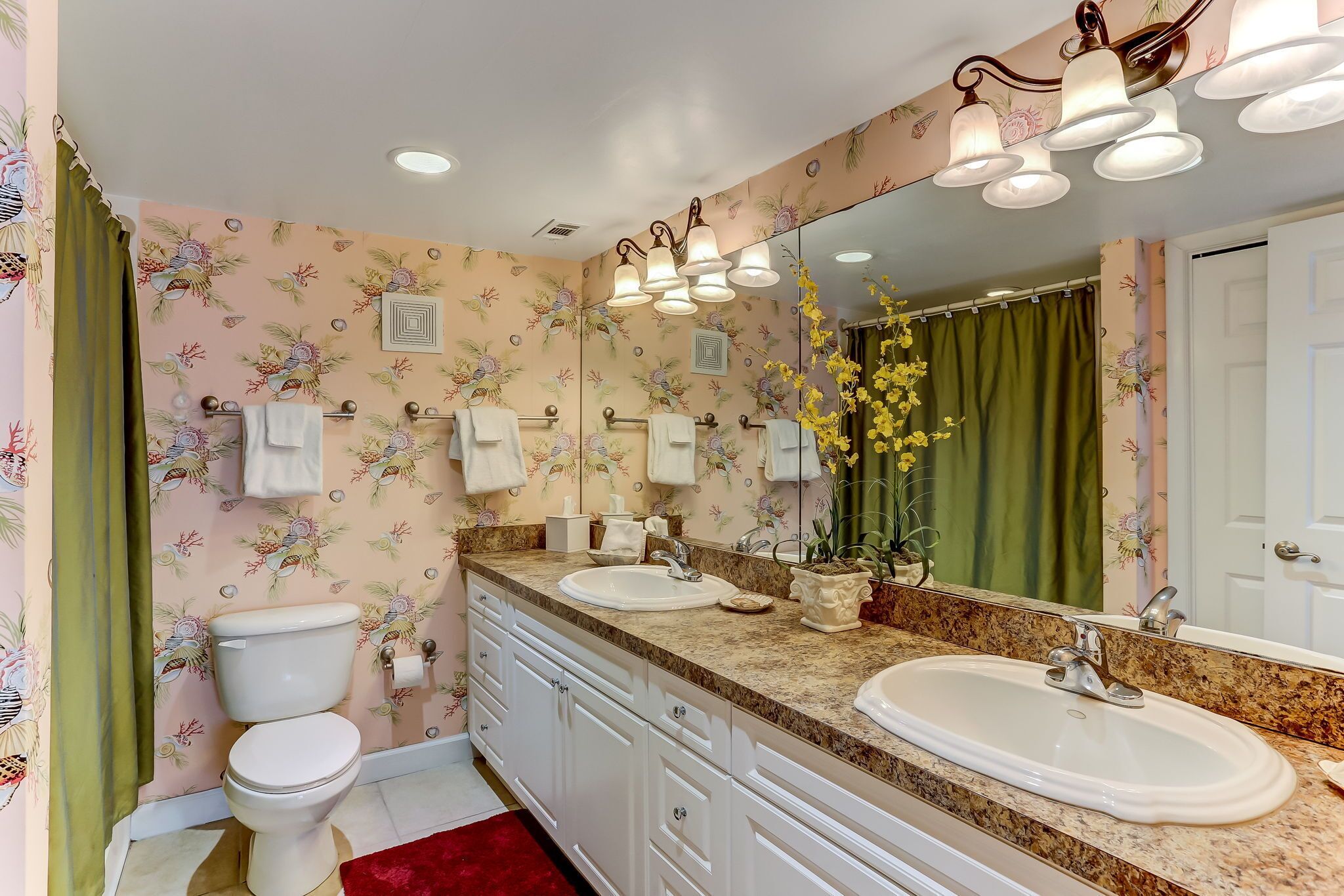 A bathroom with a toilet, two sinks, a large mirror, and a shower curtain.