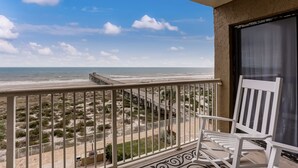 A balcony with a view of the beach, a white chair, and a wooden deck. - 446 Amelia By The Sea (Fernandina Beach)