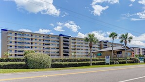 A multi-story hotel with balconies, a parking lot, and palm trees. - 446 Amelia By The Sea (Fernandina Beach)