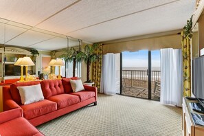 Ein Hotelzimmer mit einem roten Sofa, zwei Lampen, einem Fernseher und einem Balkon mit Vorhängen.