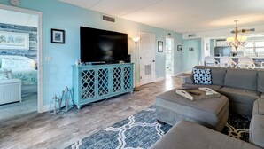 A living room with a large flat-screen TV, a teal cabinet, and a gray sectional sofa. - 438 Amelia By The Sea (Fernandina Beach)