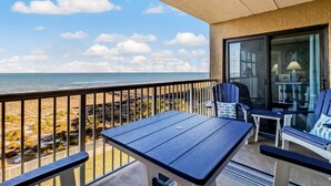 A balcony with a table and chairs, overlooking a beach with rocky terrain and the ocean. - 438 Amelia By The Sea (Fernandina Beach)