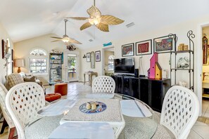 A spacious living area with a dining table, white chairs, a ceiling fan, and a TV. - 534 N Fletcher Ave #1 (Fernandina Beach)
