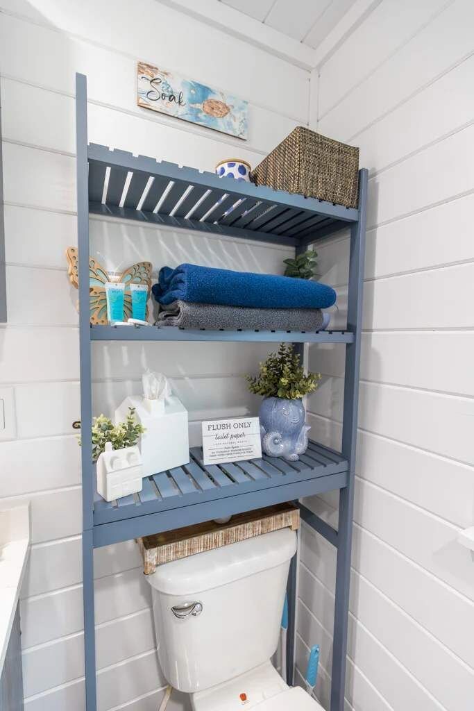 A bathroom with a blue metal shelf unit holding towels, toiletries, and a small potted plant.