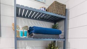 A bathroom with a blue metal shelf unit holding towels, toiletries, and a small potted plant.