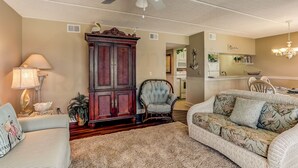 A living room with a ceiling fan, a dark wooden cabinet, a light blue armchair, and a floral sofa. - 210 Oceans of Amelia (Fernandina Beach)