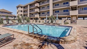 A hotel with a swimming pool, lounge chairs, and a multi-story building with balconies. - 210 Oceans of Amelia (Fernandina Beach)