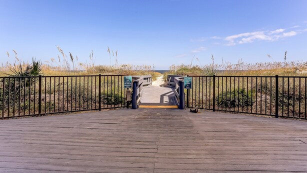 A wooden boardwalk leading to a beach with a metal fence and signs. - 210 Oceans of Amelia (Fernandina Beach)
