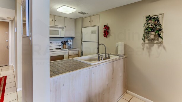 A compact kitchen with a built-in sink, white cabinets, a microwave, and a refrigerator. - 208 Sand Dollar (Fernandina Beach)