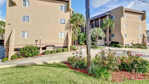 A multi-story building with a beige exterior, numbered 3056, featuring a landscaped front yard with palm trees and shrubs. - 208 Sand Dollar (Fernandina Beach)