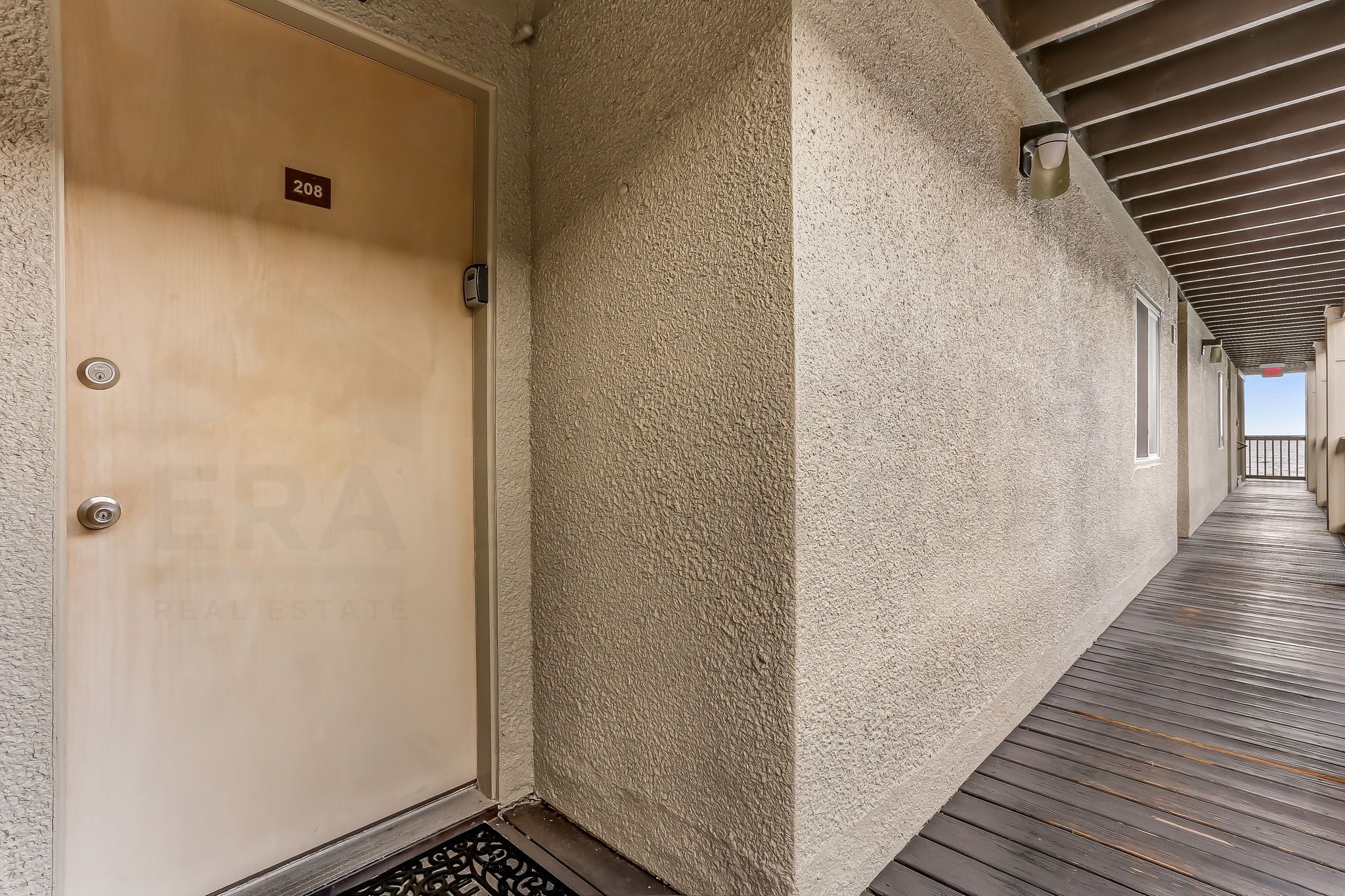A corridor with a textured wall, a wooden door labeled "208", and a metal doorbell.