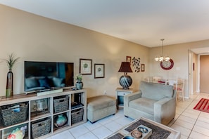 A living room with a TV, sofa, ottoman, and storage units. - 208 Sand Dollar (Fernandina Beach)