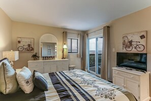A bedroom with a bed, dresser, TV, and a window with curtains. - 208 Sand Dollar (Fernandina Beach)