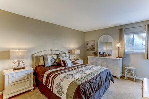 A bedroom with a bed, nightstands, dresser, mirror, and a window with blinds. - 208 Sand Dollar (Fernandina Beach)