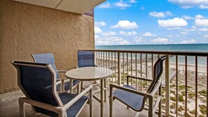 Ein Balkon mit zwei Stühlen und einem Tisch mit Blick auf einen Strand und einen Steg.
