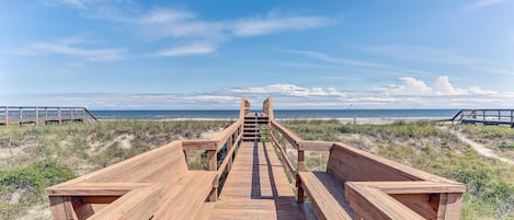 Un muelle de madera que lleva a una playa, con cielo despejado.