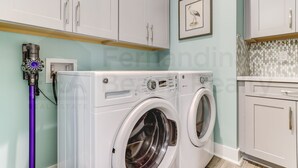 Un cuarto de lavado con dos lavadoras de carga frontal, un aspirador Dyson y armarios blancos.