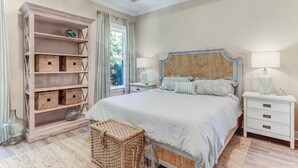 Un dormitorio con una cama grande, una mesita de noche, un aparador, una silla de mimbre y una estantería empotrada con cajas de almacenamiento.