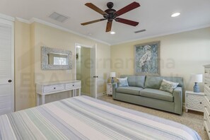 Un dormitorio con cama, sofá verde, ventilador de techo, un cuadro y cómoda.