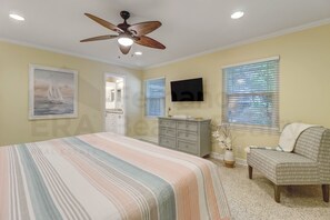 Une chambre à coucher comprenant un lit, une chaise, une commode, un téléviseur et un ventilateur de plafond.