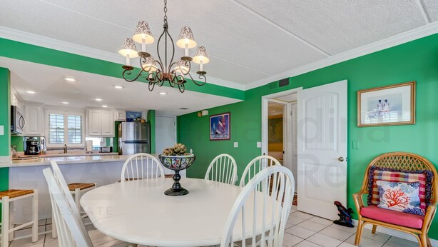 A dining area with a white table and chairs, a chandelier, and a green wall. - A1 Amelia South (Fernandina Beach)