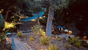 A garden pathway with a swing set and a play area, surrounded by trees and illuminated by string lights. - 3046 Skycrest Drive (Fallbrook)