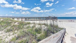 Una banchina di legno che si protende su una spiaggia sabbiosa, con un cielo azzurro limpido.