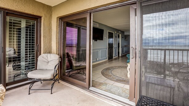 Una stanza con una porta scorrevole in vetro che dà su un balcone, una poltrona imbottita e un tappeto decorato.