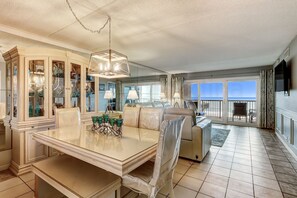 A dining area with a glass table, chairs, and a cabinet with glass doors. - 550 Amelia By The Sea (Fernandina Beach)