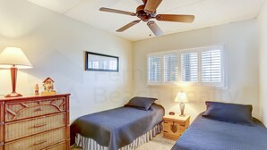 Slaapkamer met twee bedden, een plafondventilator, een dressoir en een raam met zonwering.