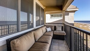 Een balkon met een beige bank, een rieten stoel en uitzicht op het strand.