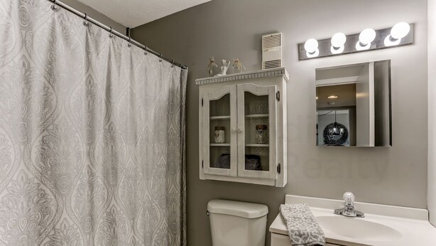 Une salle de bain comprenant des toilettes, un lavabo, un meuble avec des portes en verre et un rideau de douche.