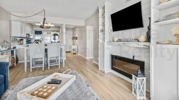 Een moderne woonkamer met een open haard, een flatscreen televisie en een eethoek, met een keuken op de achtergrond.