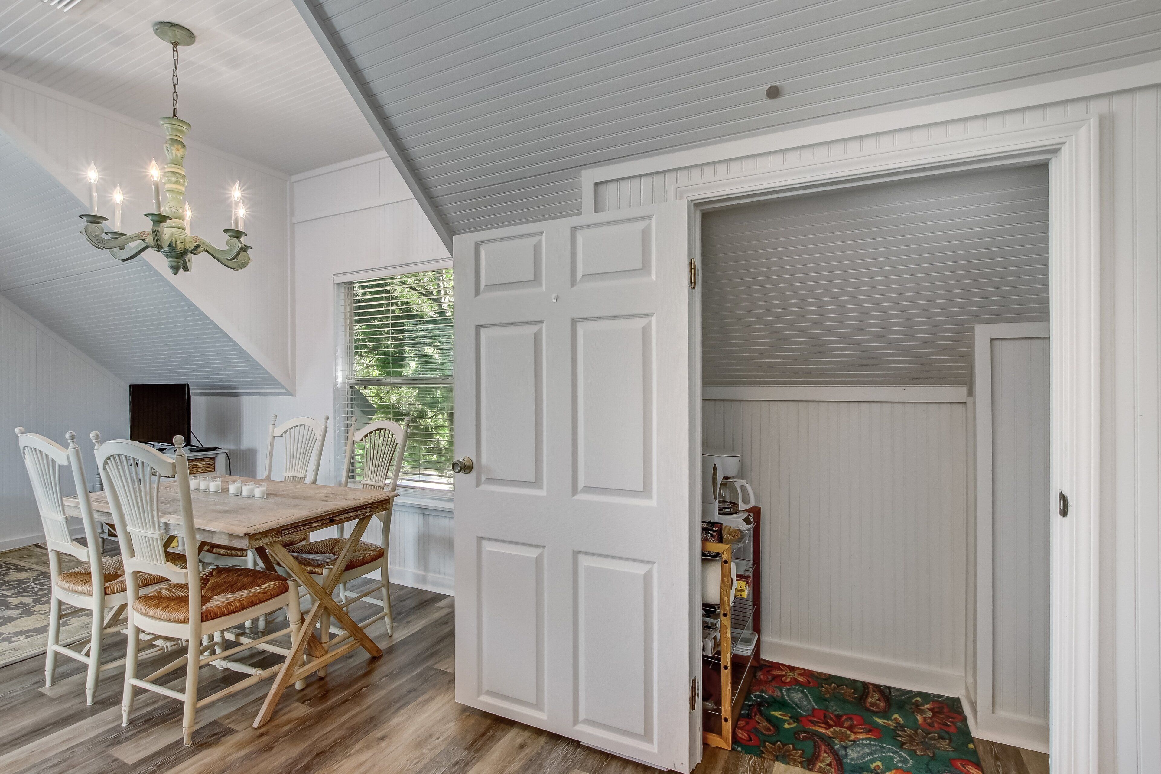 A dining area with a wooden table and chairs, a chandelier, and a partially open door leading to a closet.
