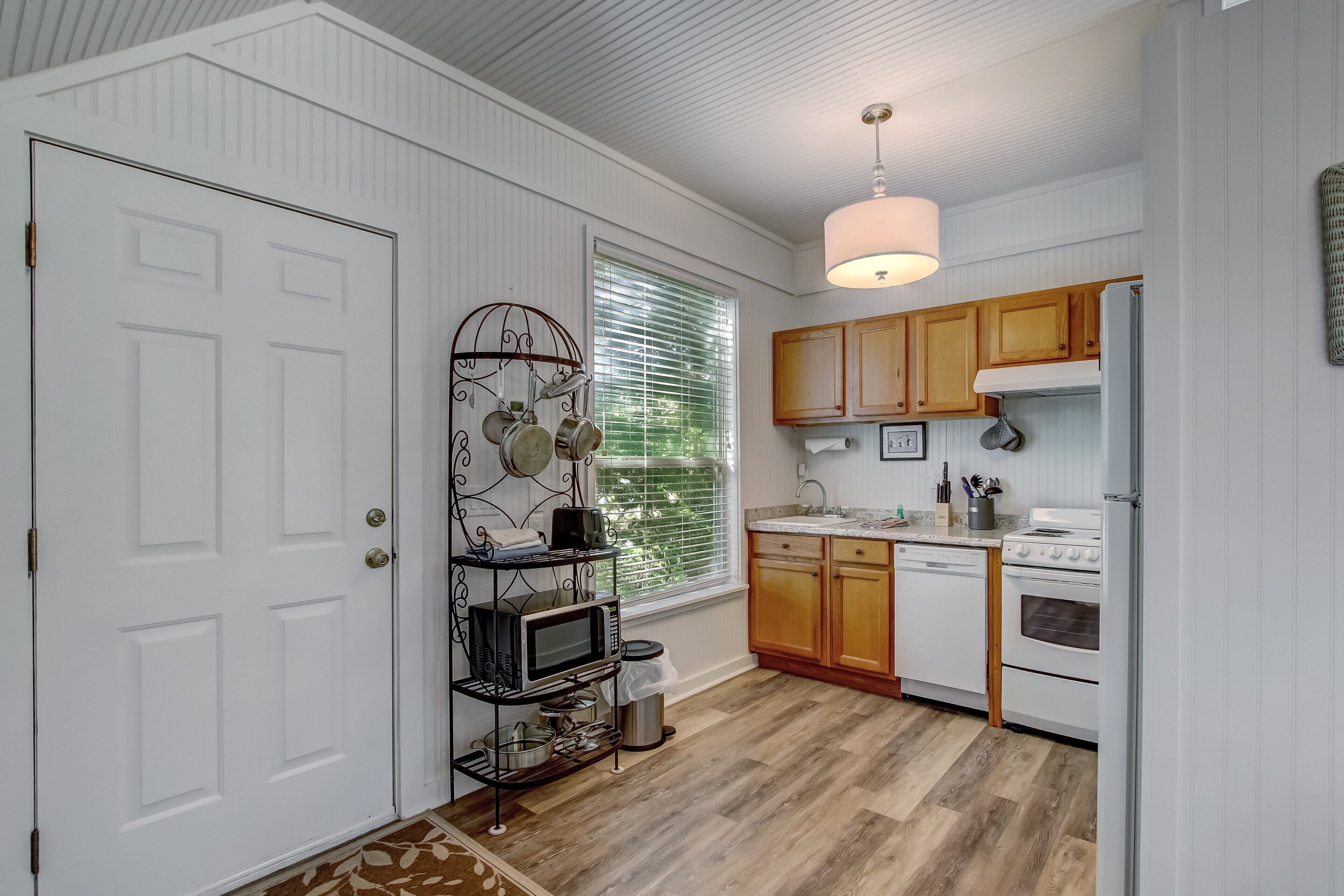 A compact kitchen with white cabinetry, a microwave, a stove, and a hanging pot rack.