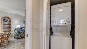 Ein Waschraum mit einer weißen Waschmaschine und einem Trockner, einem Holzstuhl, einem Tisch und einem gemusterten Sofa im Hintergrund.