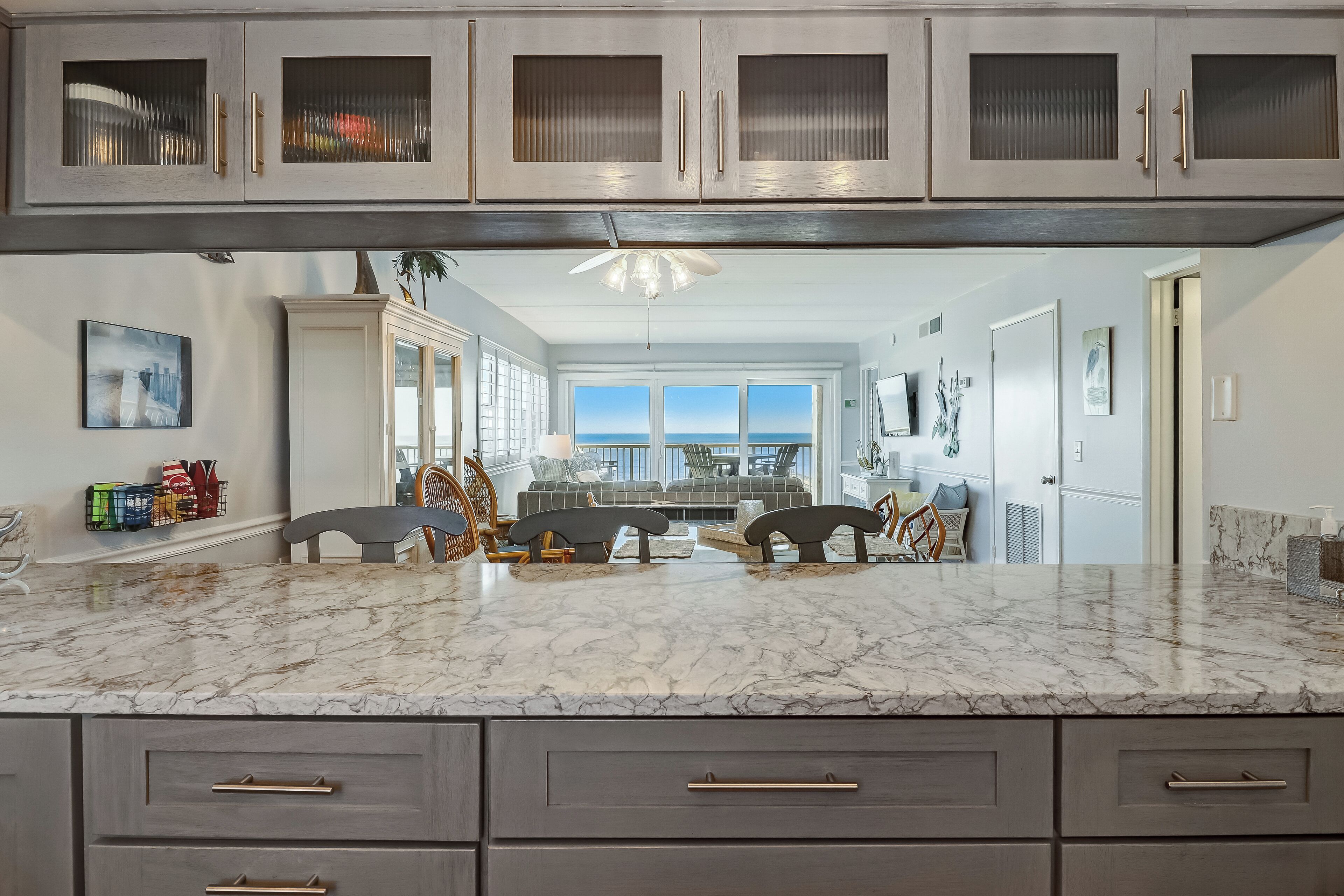 A kitchen with marble countertops, dark cabinetry, and a view to the living area.